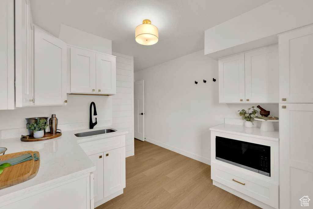 Kitchen with a sink, built in microwave, light wood-type flooring, and white cabinets