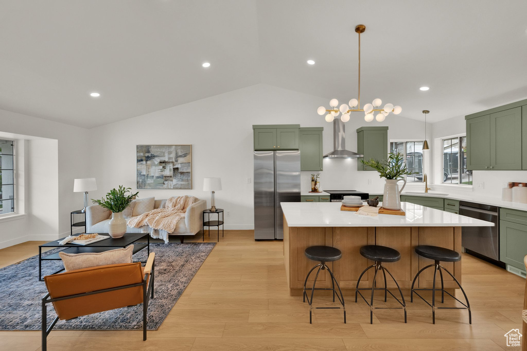 Kitchen with green cabinets, appliances with stainless steel finishes, wall chimney range hood, vaulted ceiling, and light countertops