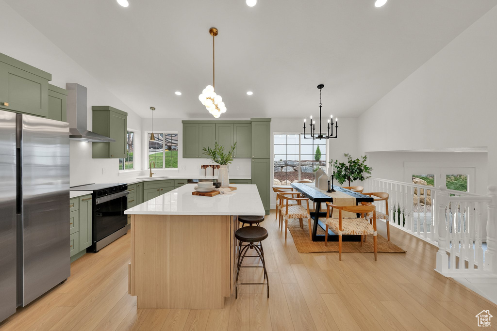 Kitchen with green cabinetry, electric stove, wall chimney exhaust hood, a sink, and freestanding refrigerator