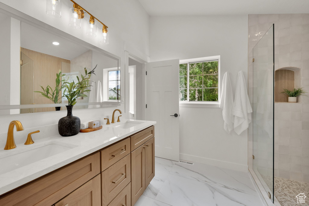 Full bath with tiled shower, double vanity, marble finish flooring, and recessed lighting