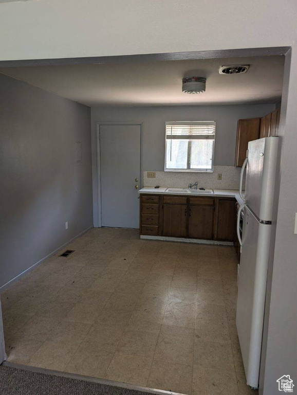 Kitchen with freestanding refrigerator, light countertops, a sink, backsplash, and brown cabinetry