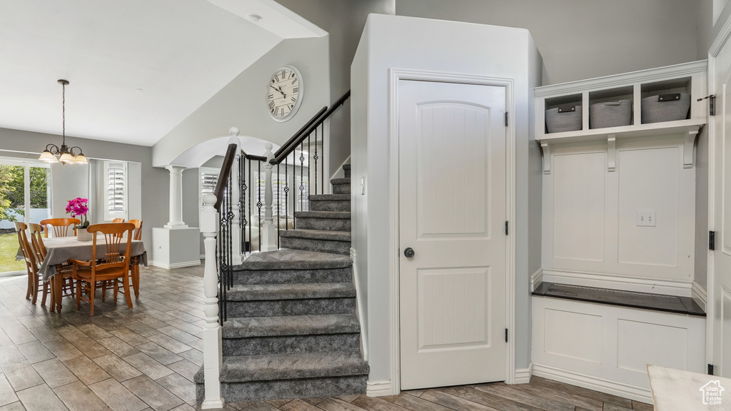 Staircase featuring lofted ceiling, wood finished floors, ornate columns, a chandelier, and baseboards