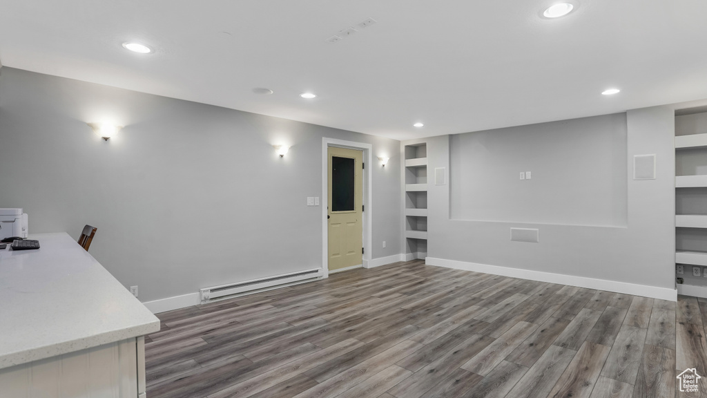 Unfurnished living room featuring a baseboard heating unit, recessed lighting, built in shelves, wood finished floors, and baseboards