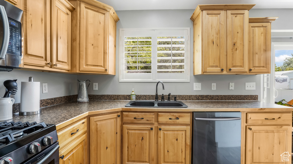 Kitchen with stainless steel appliances, a sink, dark countertops, and light brown cabinetry