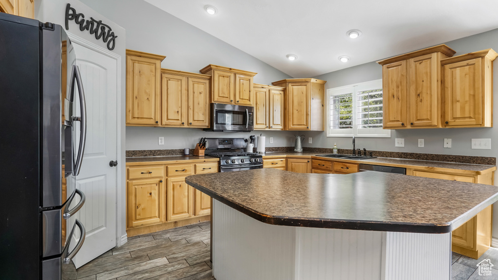 Kitchen featuring stainless steel appliances, dark countertops, lofted ceiling, a sink, and wood finish floors