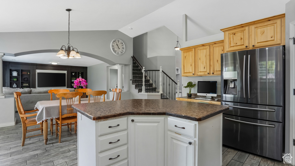 Kitchen featuring stainless steel fridge with ice dispenser, vaulted ceiling, arched walkways, dark countertops, and light wood finished floors