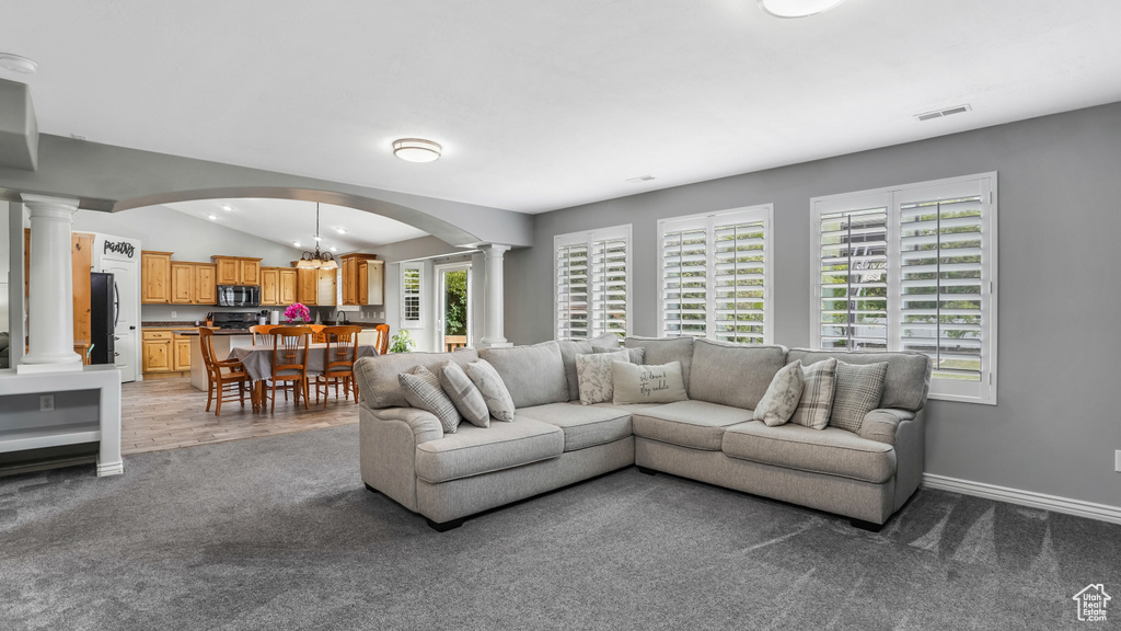 Living area featuring decorative columns, arched walkways, carpet flooring, a chandelier, and vaulted ceiling