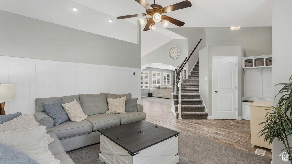 Living area with arched walkways, ceiling fan, stairway, wood finished floors, and a decorative wall