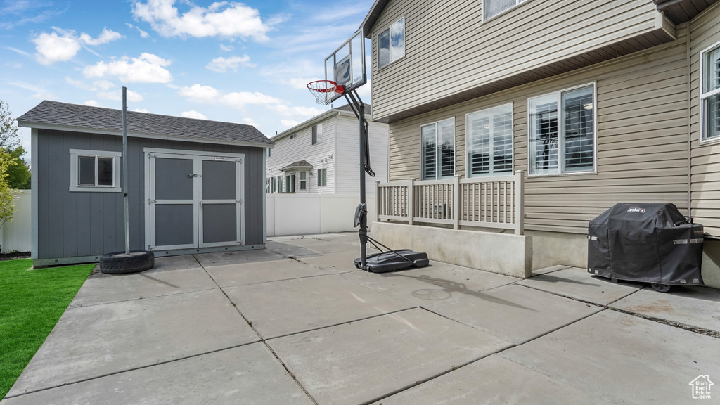 View of patio with a storage shed, an outdoor structure, a grill, and fence