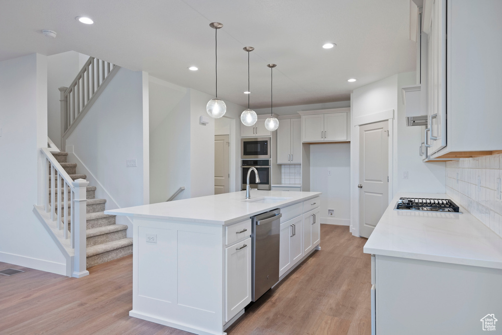 Kitchen featuring stainless steel appliances, tasteful backsplash, light wood-style floors, white cabinetry, and recessed lighting