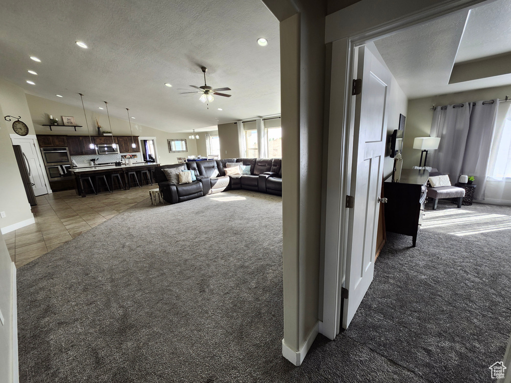Carpeted living room featuring lofted ceiling, recessed lighting, a ceiling fan, baseboards, and a textured ceiling