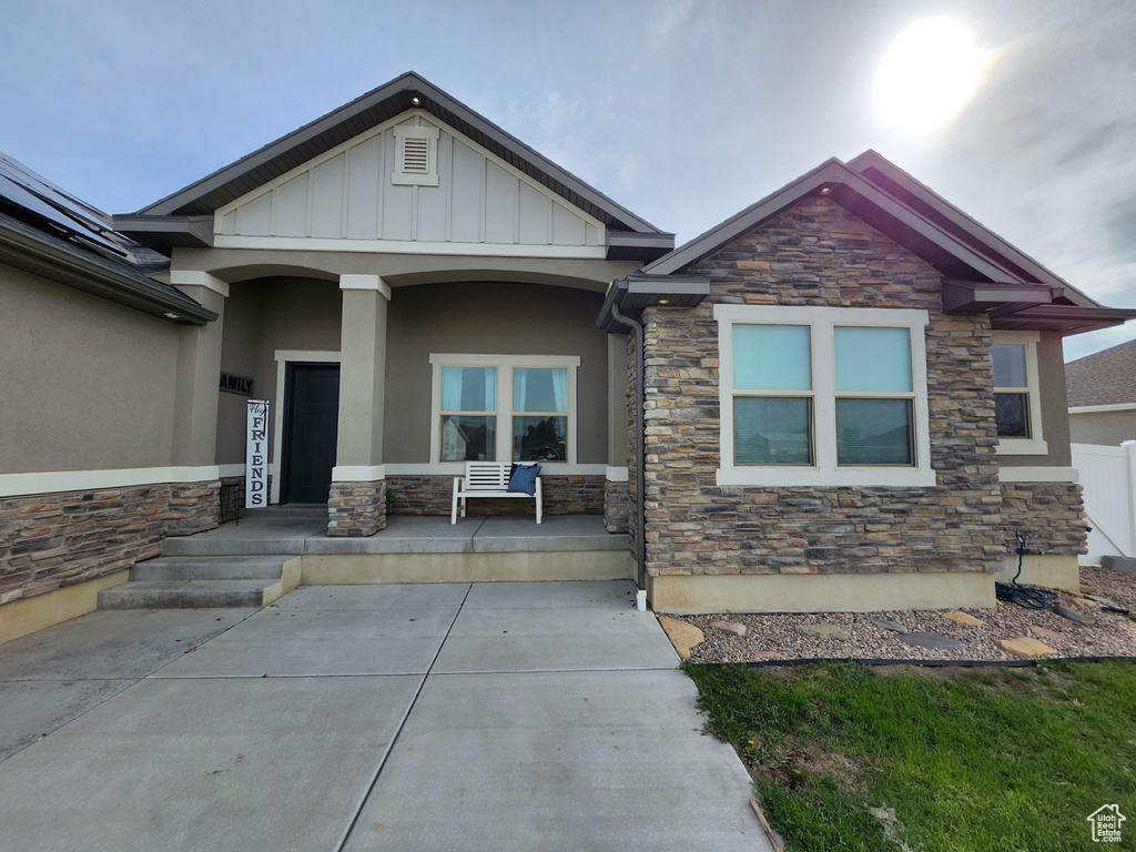 View of front of house with stone siding, covered porch, stucco siding, and board and batten siding