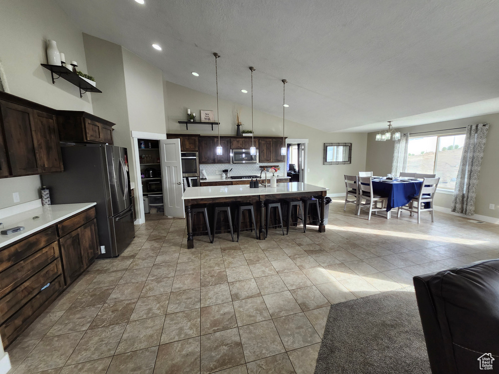Kitchen with appliances with stainless steel finishes, a breakfast bar, dark brown cabinets, light countertops, and a chandelier