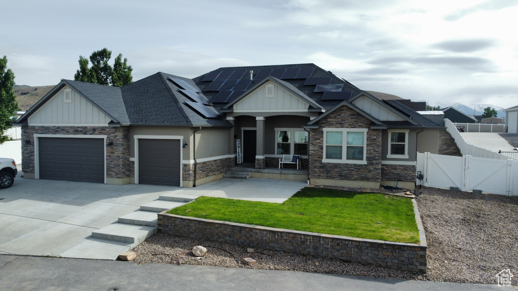 Craftsman house featuring board and batten siding, a gate, a garage, a porch, and roof mounted solar panels