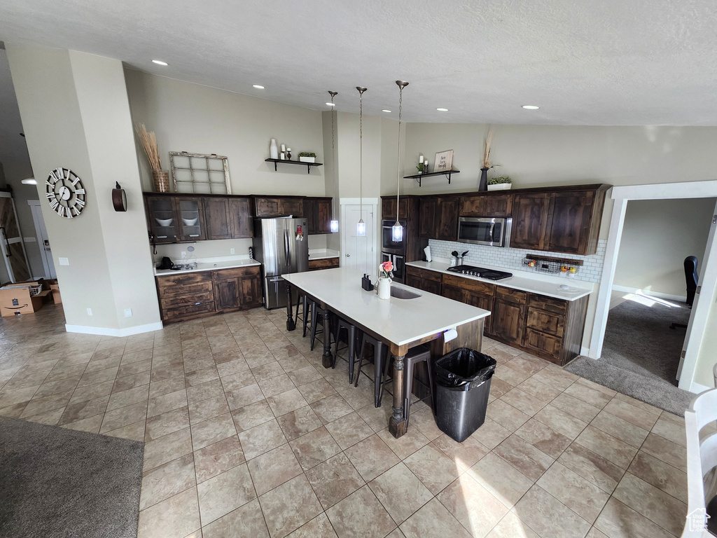Kitchen with appliances with stainless steel finishes, a breakfast bar, decorative backsplash, dark brown cabinetry, and light countertops