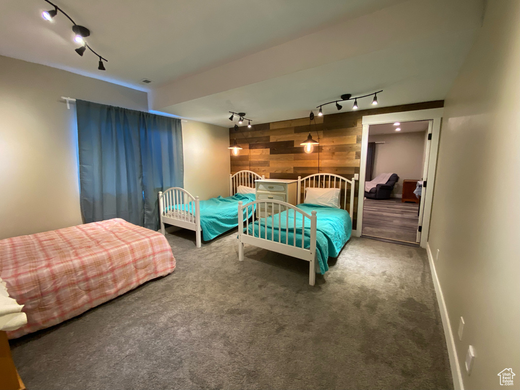 Bedroom featuring rail lighting, wood walls, carpet flooring, an accent wall, and baseboards