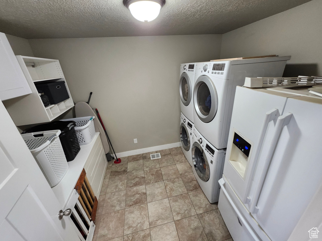 Washroom with stacked washer and clothes dryer, a textured ceiling, and baseboards