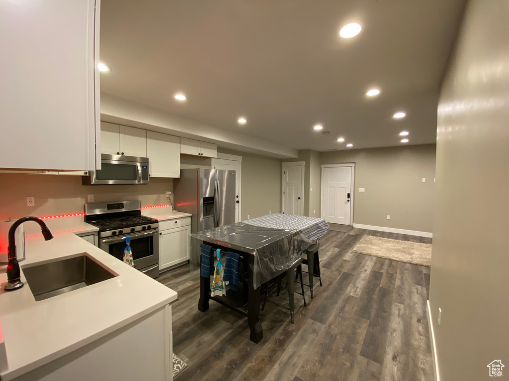 Kitchen featuring appliances with stainless steel finishes, a sink, recessed lighting, white cabinetry, and dark wood finished floors