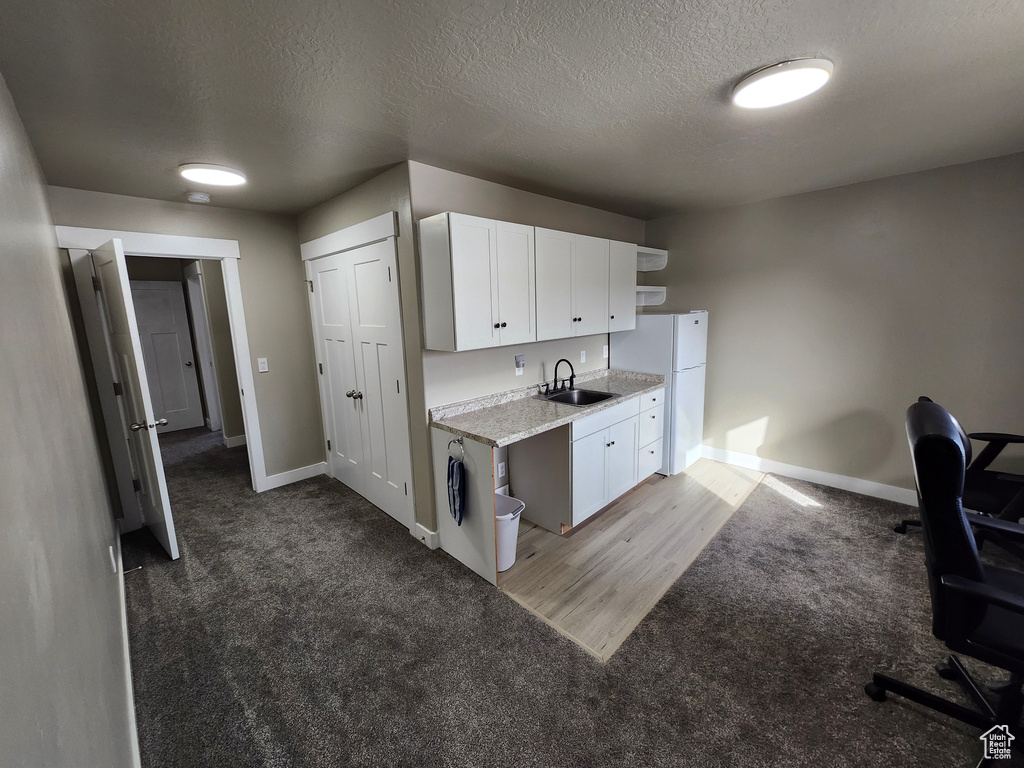 Kitchen featuring freestanding refrigerator, a sink, light carpet, baseboards, and a textured ceiling