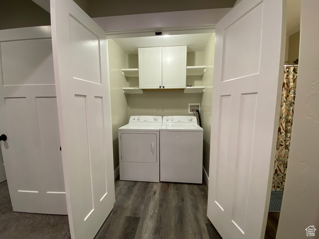 Clothes washing area featuring cabinet space, washing machine and clothes dryer, and dark wood-style floors