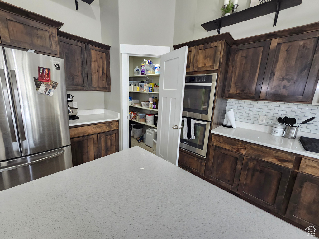 Kitchen with appliances with stainless steel finishes, light countertops, decorative backsplash, and dark brown cabinetry