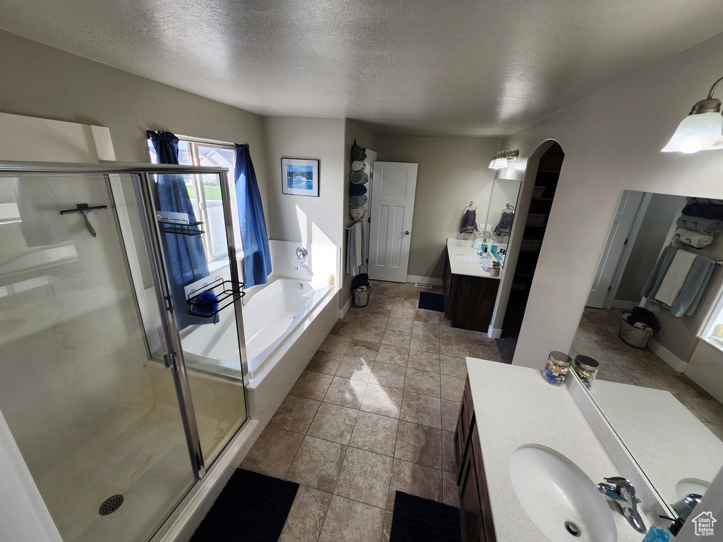 Bathroom with a shower stall, a bath, two vanities, a textured ceiling, and baseboards