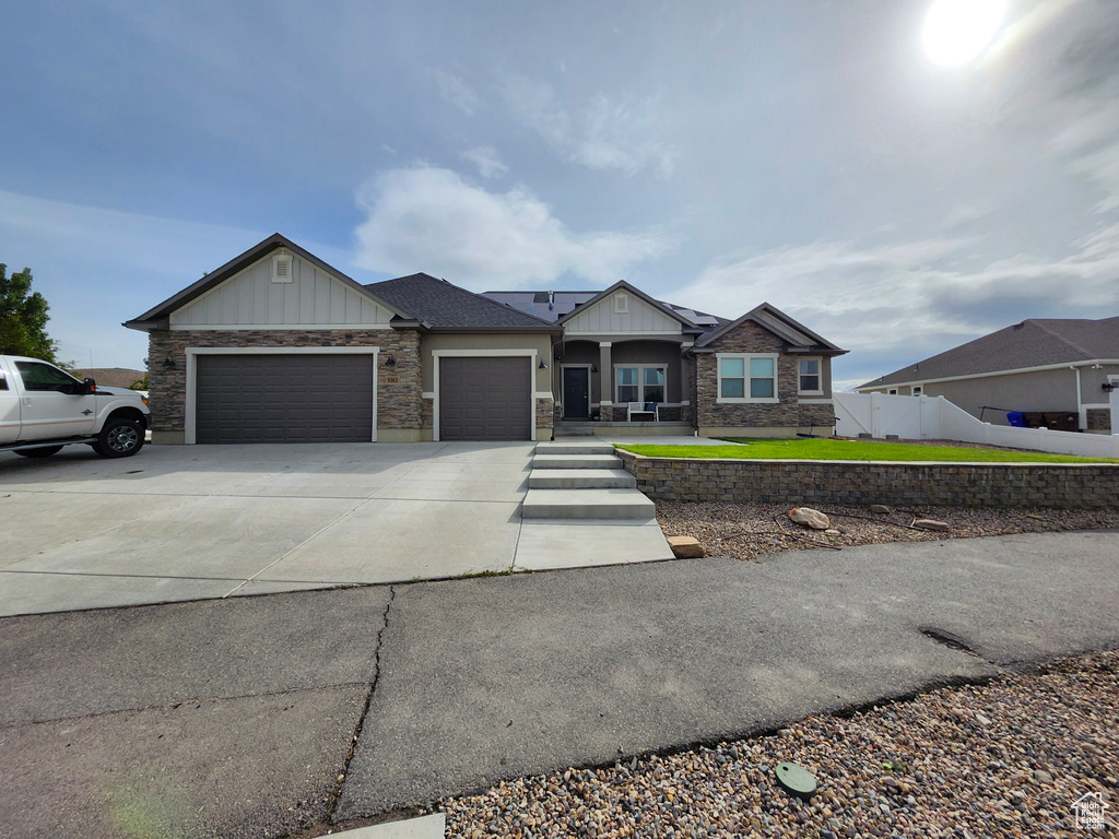 View of front facade featuring board and batten siding, an attached garage, concrete driveway, fence, and stone siding