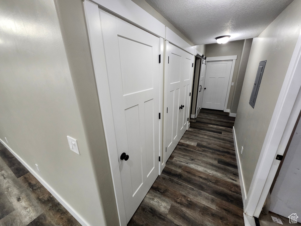 Corridor featuring dark wood-type flooring, a textured ceiling, baseboards, and a barn door