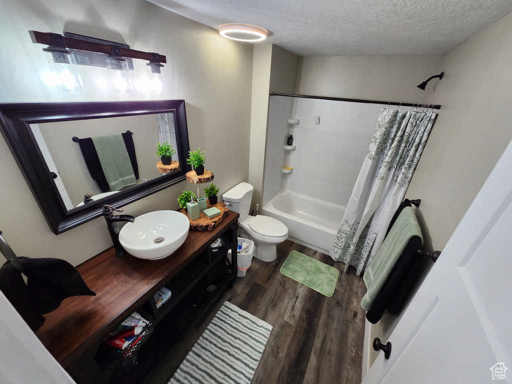 Bathroom with a textured ceiling, wood finished floors, toilet, shower / bath combo, and vanity