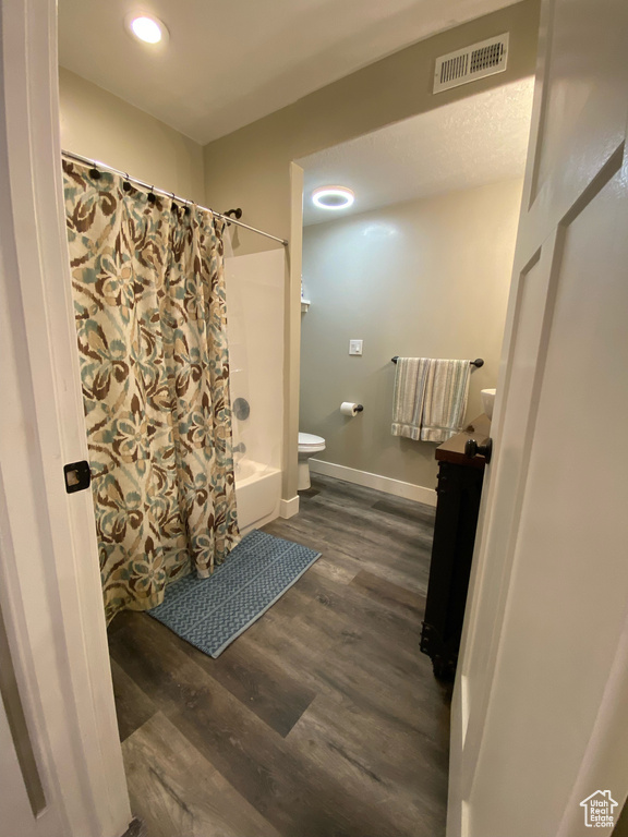 Full bathroom featuring toilet, wood finished floors, shower / bath combo with shower curtain, baseboards, and recessed lighting