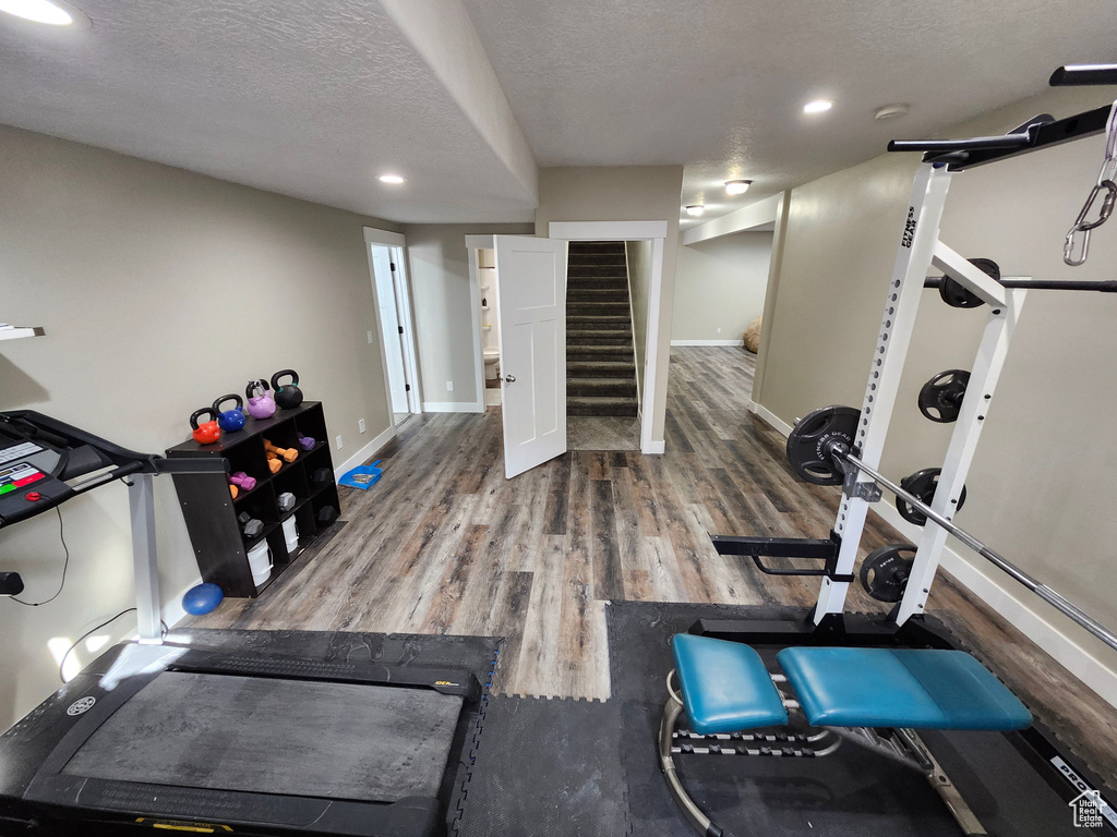 Exercise area featuring wood finished floors, baseboards, a textured ceiling, and recessed lighting