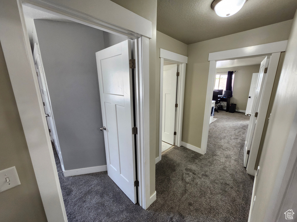 Hall with dark colored carpet, baseboards, and a textured ceiling