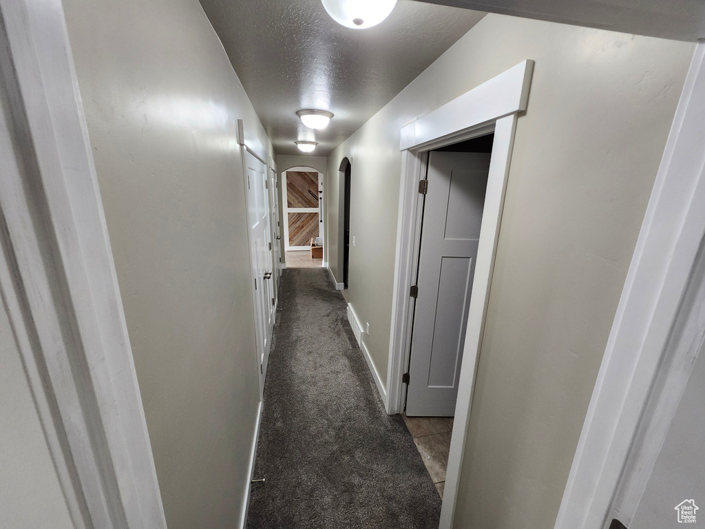 Corridor with arched walkways, a textured ceiling, carpet flooring, and baseboards