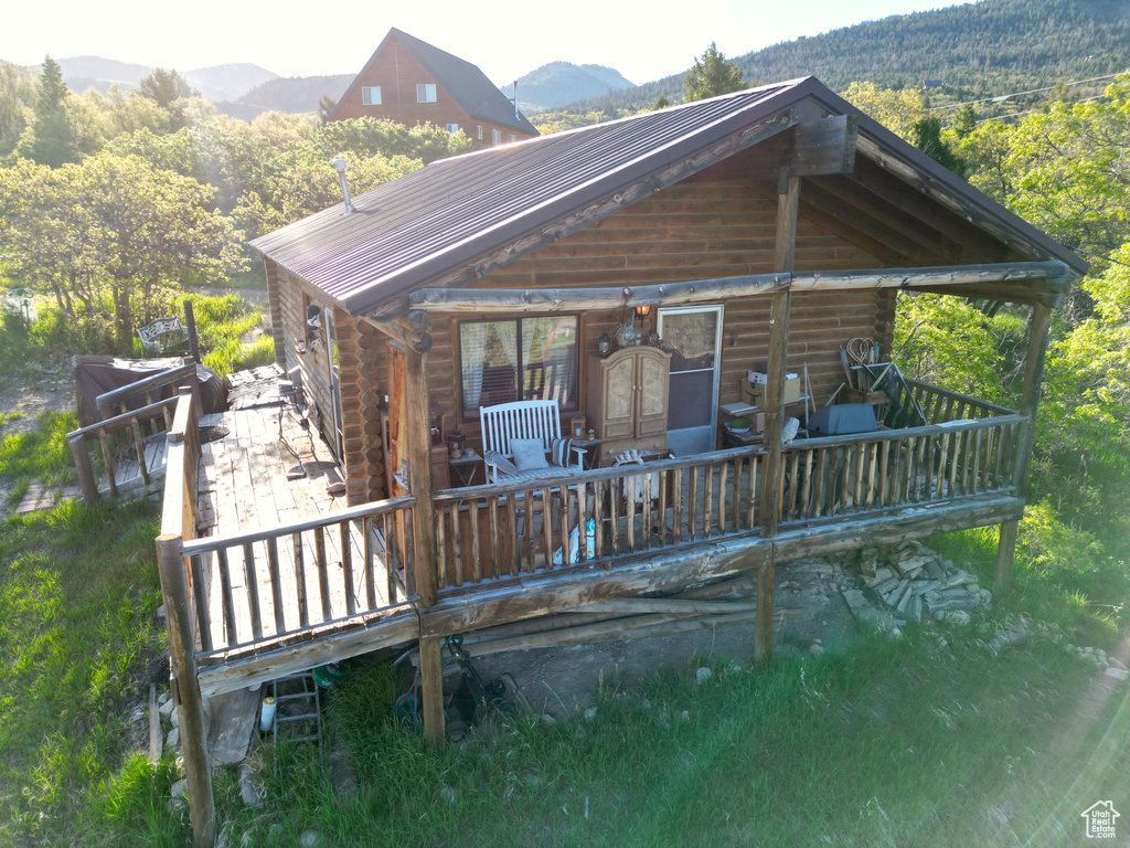 Back of property featuring log siding, metal roof, a deck with mountain view, and a wooded view
