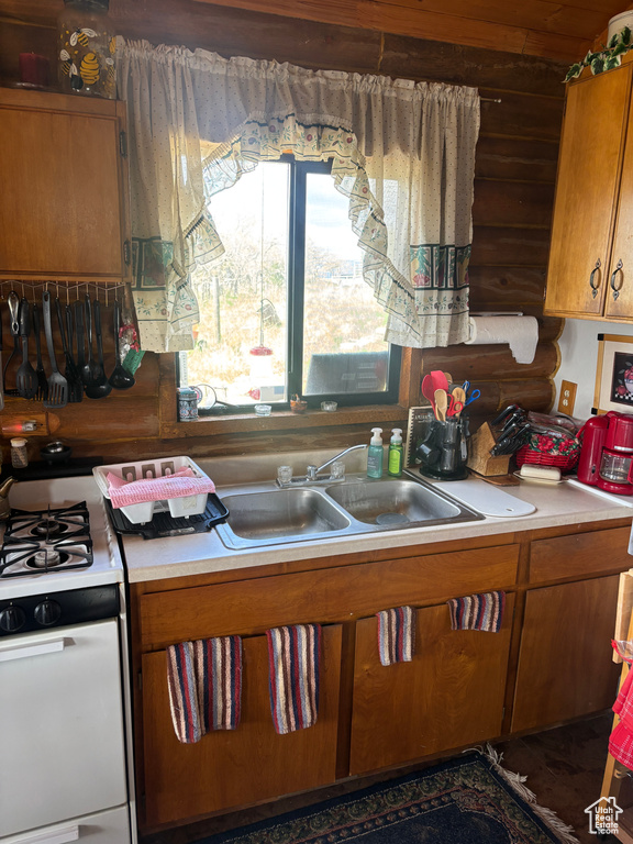 Kitchen featuring brown cabinets, gas range oven, light countertops, a sink, and log walls