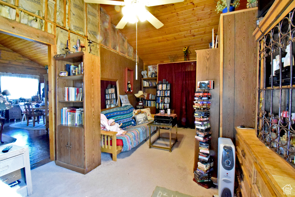 Carpeted living area with lofted ceiling, a ceiling fan, wooden ceiling, and wooden walls