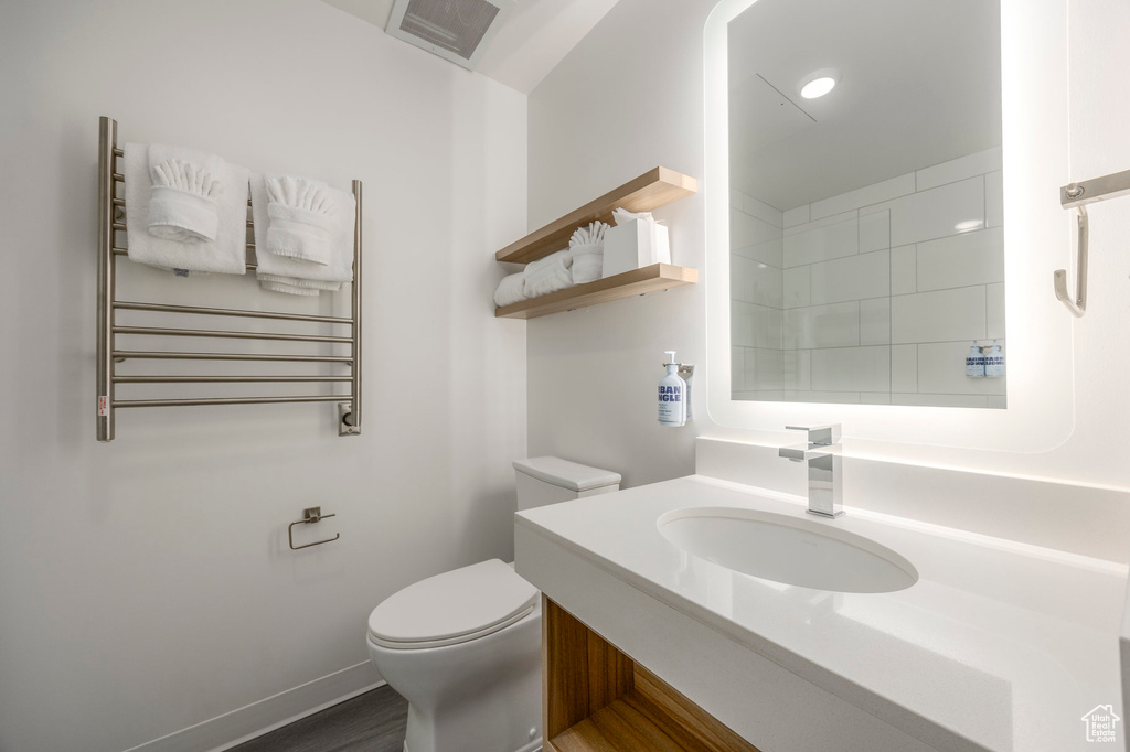 Bathroom with radiator heating unit, toilet, vanity, and baseboards