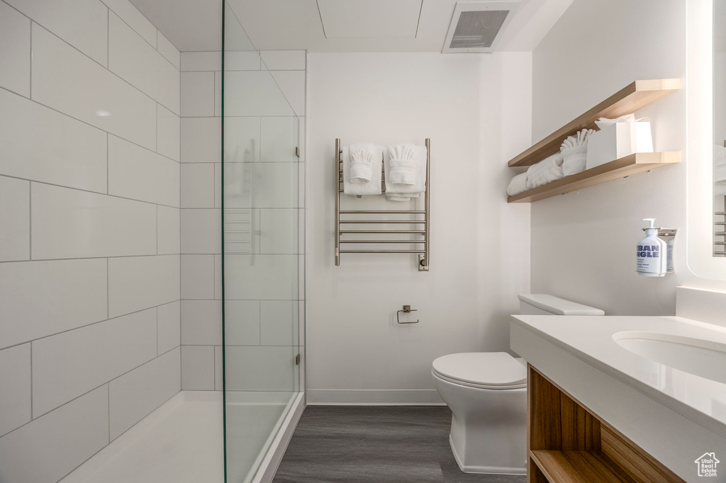 Bathroom with wood finished floors, toilet, baseboards, tiled shower, and vanity