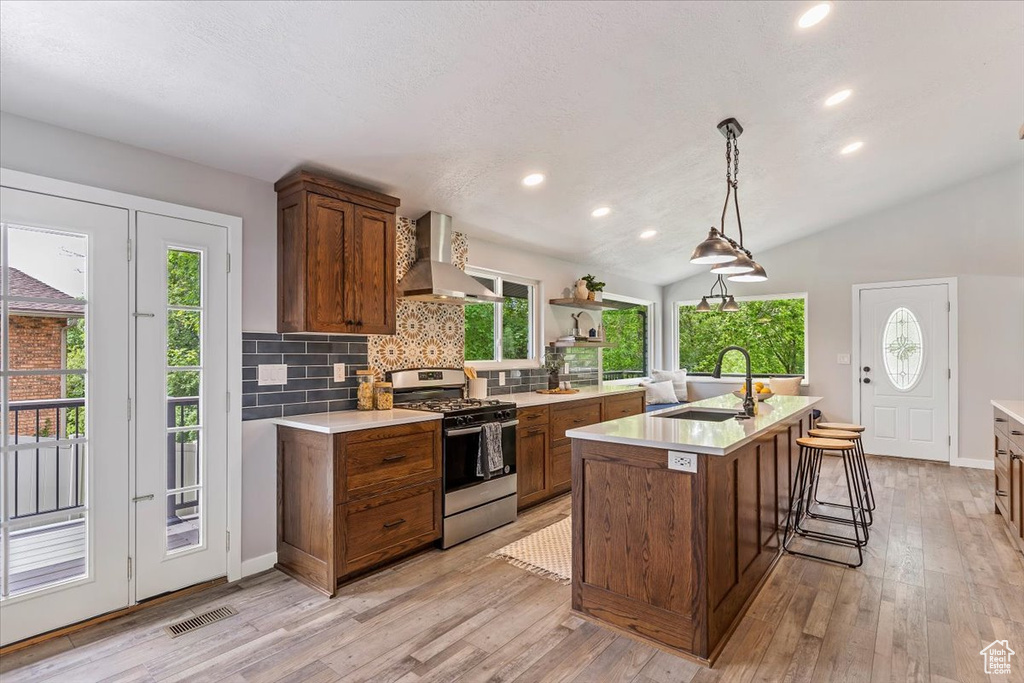 Kitchen featuring gas stove, wall chimney exhaust hood, a sink, light countertops, and decorative backsplash
