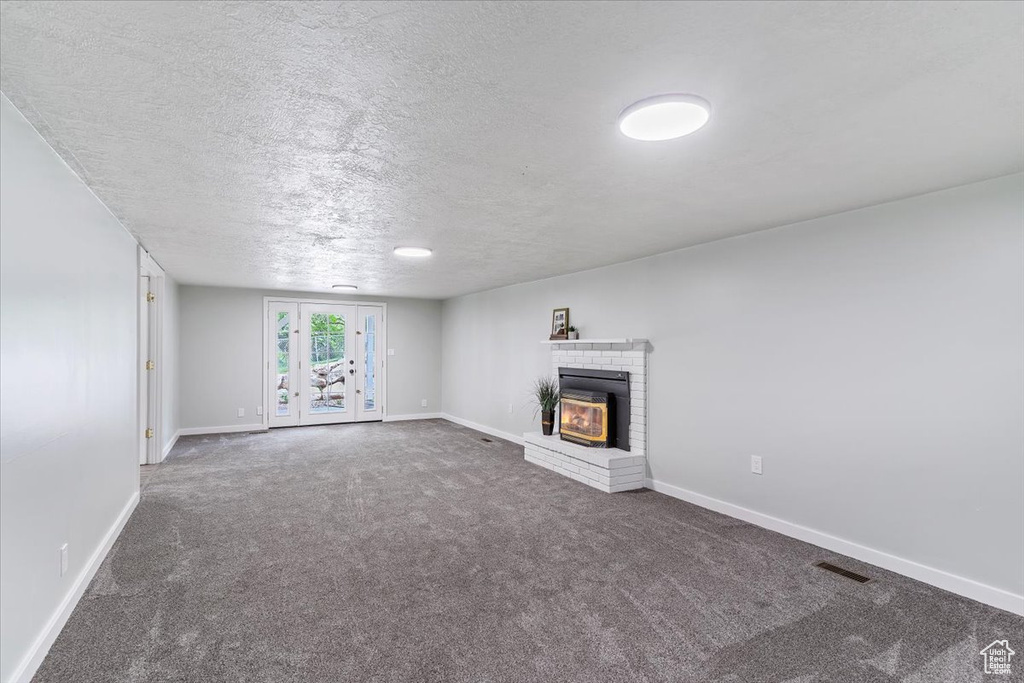 Unfurnished living room with carpet, baseboards, a textured ceiling, and a fireplace