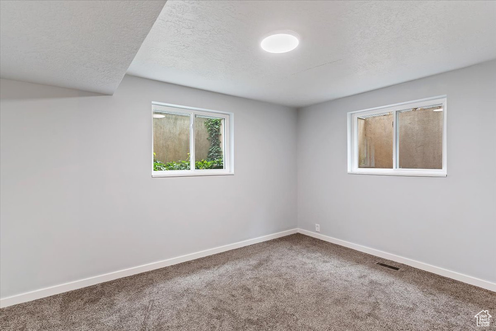 Carpeted empty room with a textured ceiling and baseboards