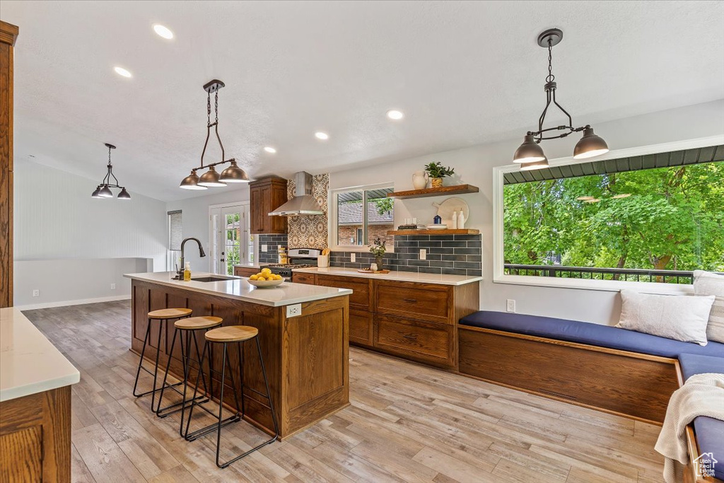 Kitchen with wall chimney range hood, a sink, brown cabinetry, stainless steel range with gas cooktop, and tasteful backsplash