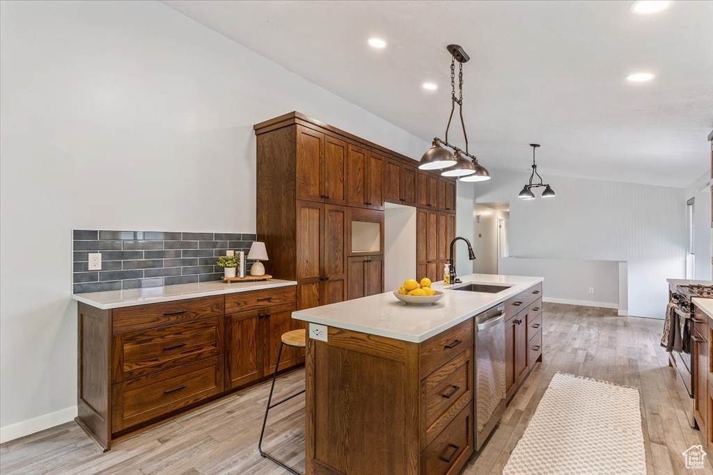 Kitchen with a sink, stainless steel appliances, a center island with sink, backsplash, and brown cabinetry