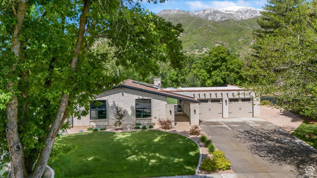 View of front of property featuring an attached garage, a mountain view, concrete driveway, solar panels, and a front yard