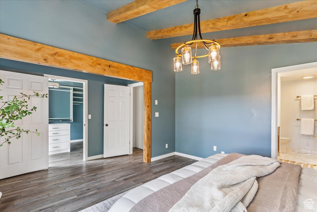 Bedroom with beamed ceiling, dark wood finished floors, baseboards, ensuite bathroom, and a chandelier