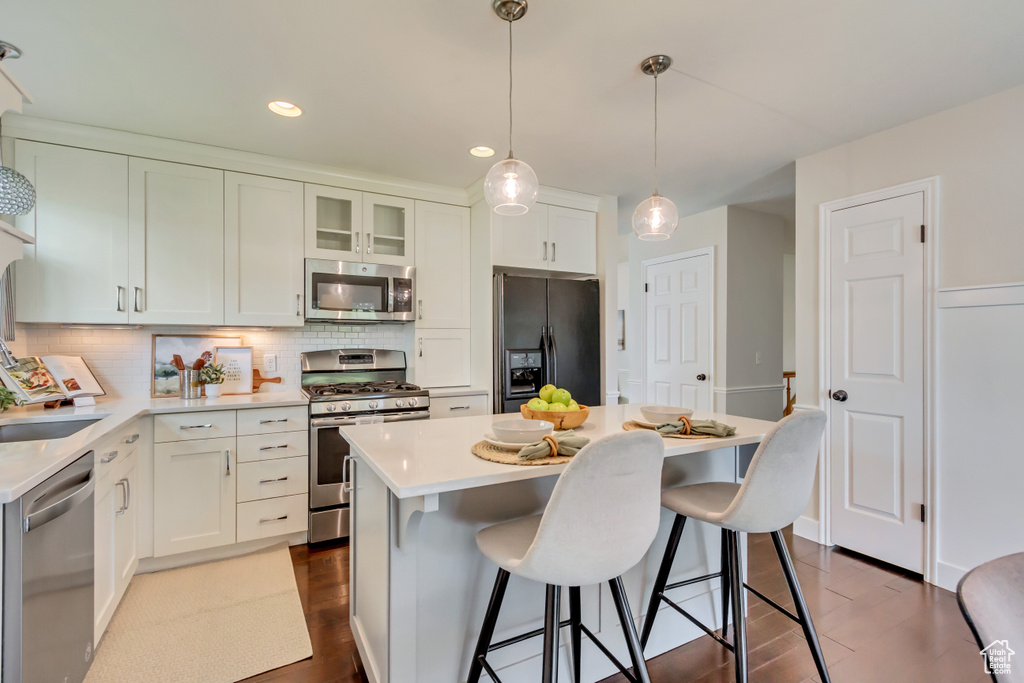Kitchen featuring appliances with stainless steel finishes, dark wood-type flooring, light countertops, decorative backsplash, and recessed lighting