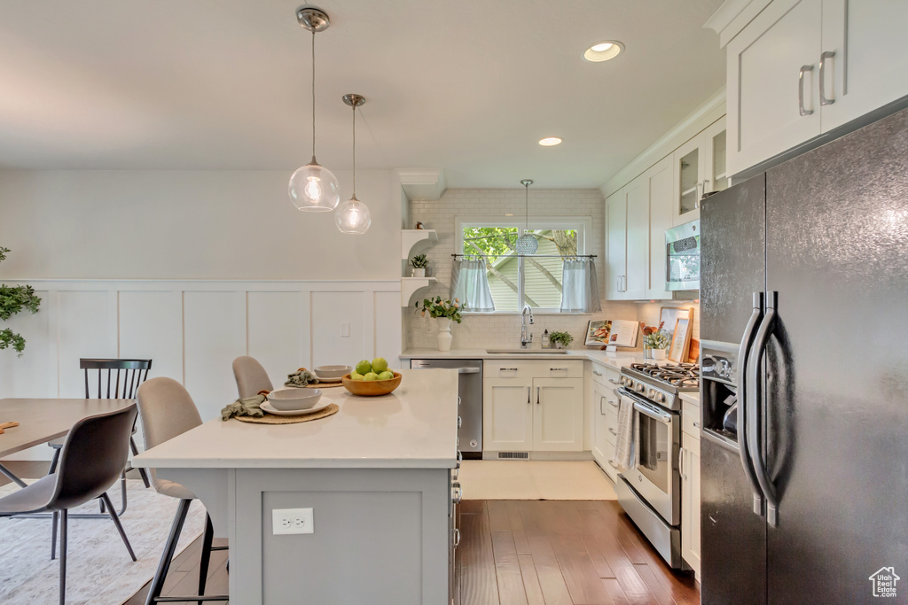 Kitchen with appliances with stainless steel finishes, a sink, hardwood / wood-style floors, light countertops, and a kitchen breakfast bar