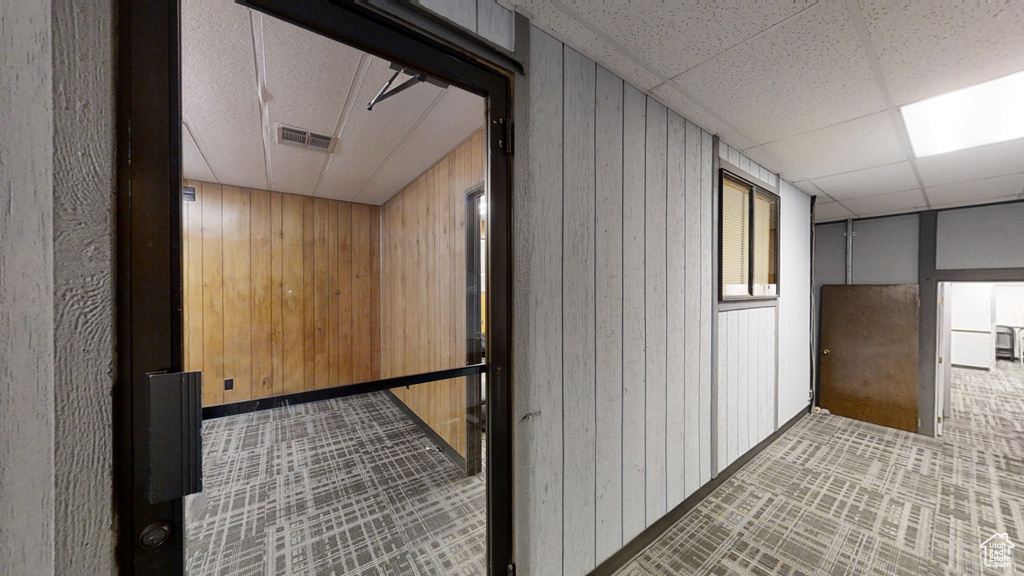 Hall featuring wooden walls and a drop ceiling