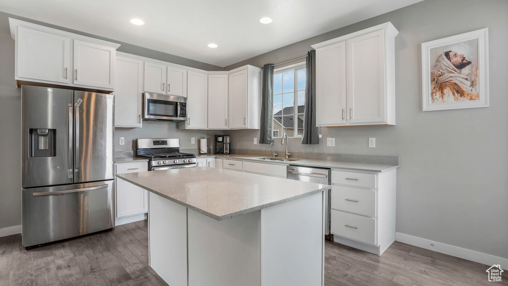 Kitchen with appliances with stainless steel finishes, a sink, baseboards, wood finished floors, and recessed lighting