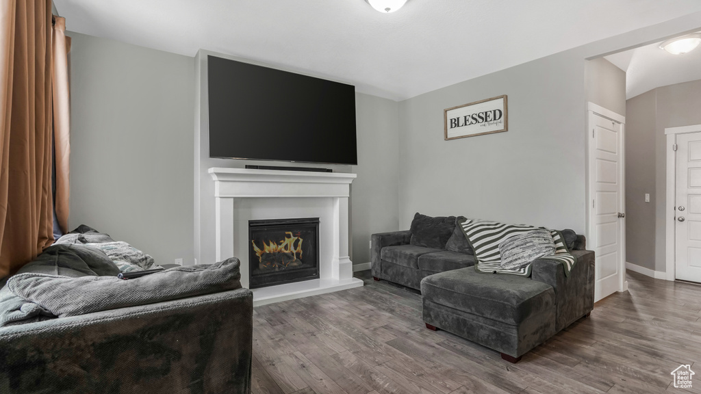 Living room with wood finished floors, a lit fireplace, and baseboards